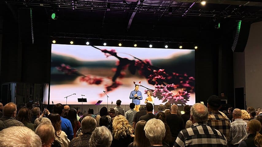 Congregation worshiping with stage lighting and an LED video wall